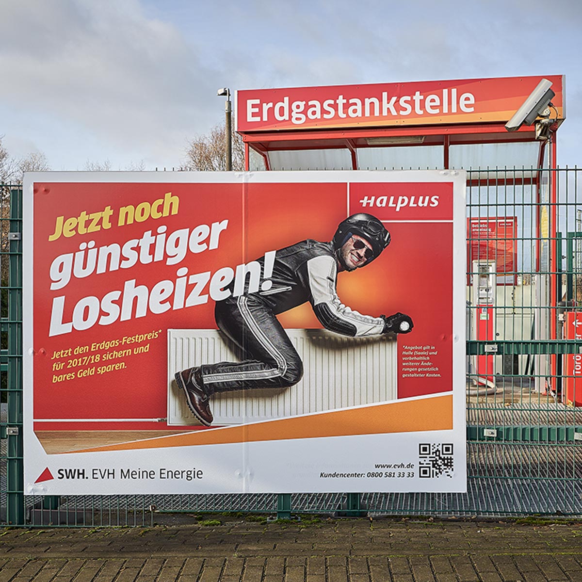 Plakat an der Erdgastankstelle in der Freiimfelder Straße für EVH Halle: Kampagne „Jetzt noch günstiger Losheizen!" Werbemotiv: Mann fährt Motorrad auf Heizungskörper